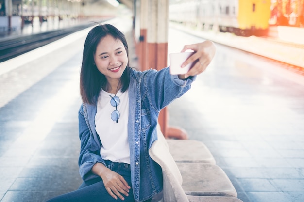 Woman taking selfie photo using her cellphone while sitting on a wooden bench