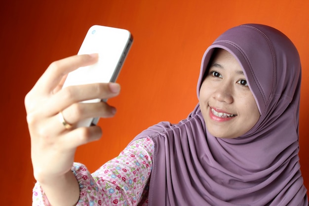 Woman taking selfie standing against orange background