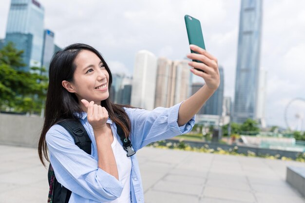 Женщина делает селфи с мобильным телефоном с любовным жестом пальца в Гонконге