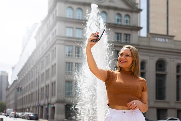 南アメリカの美しい噴水の背景にスマートフォンで自分撮りをする女性