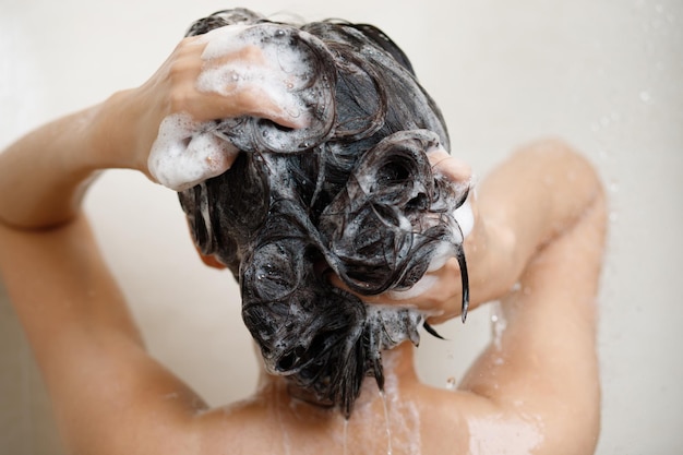 Женщина принимает душ и моет волосы шампунем