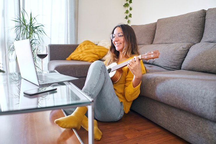 Photo woman taking ukulele lessons online from her laptop during covid quarantine.