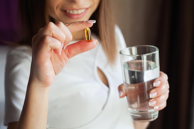 Woman taking vitamin pill with glass of fresh water indoors