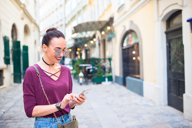 女性は都市で彼女のスマートフォンで話します。イタリアの都市で屋外の若い魅力的な観光客