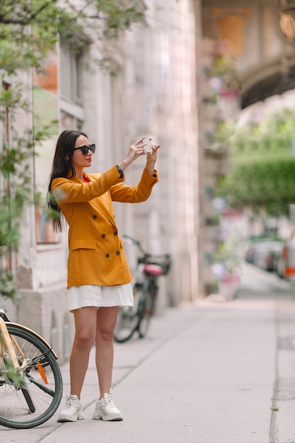 女性は都市で彼女のスマートフォンで話します。イタリアの都市で屋外の若い魅力的な観光客