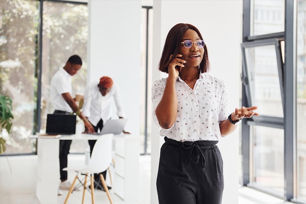 Woman talking by phone Group of african american business people working in office together