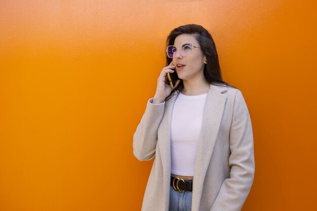 A woman talking on a cell phone against a orange wall