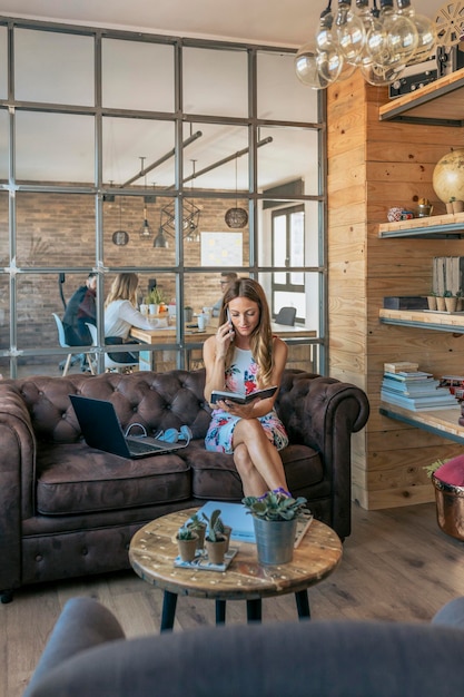 Woman talking on the cellphone working sitting on a sofa