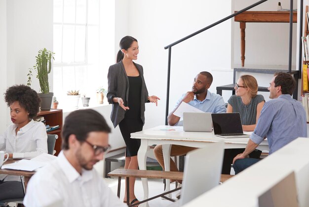 Woman talking to colleagues at a desk in open plan office