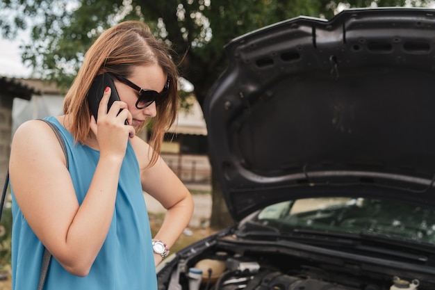 Foto donna che parla al cellulare mentre si trova accanto a un'auto in rovina sulla strada