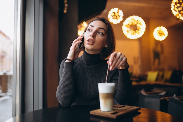 電話で話し、カフェでコーヒーを飲む女性