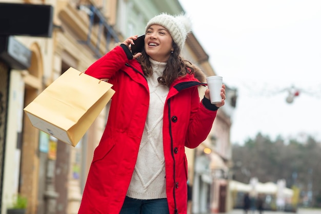 Woman talking on phone and holding cup of tea at winter street