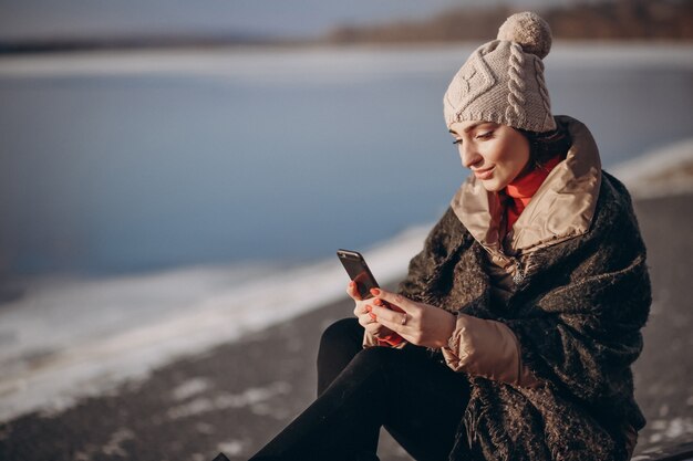 Woman talking on the phone and sitting on a bench by the lake