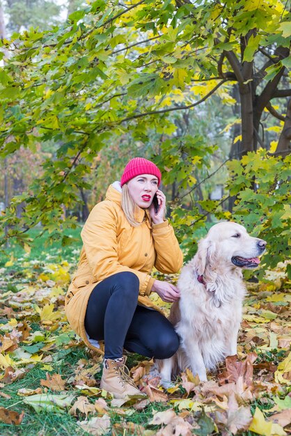 woman talking  on the phone while walking with her retriever among yellow autumn leaves