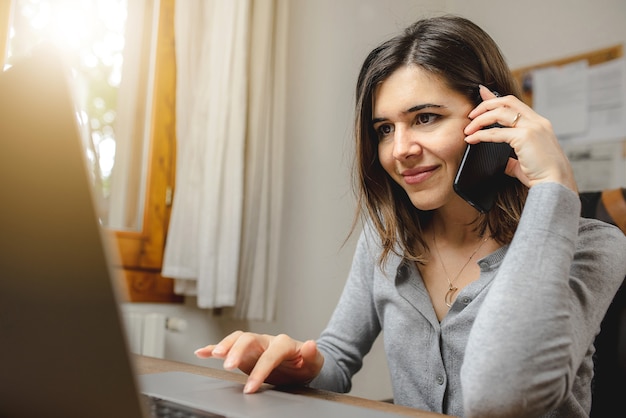 woman talking on the phone while working on computer in desk office. Searching on internet