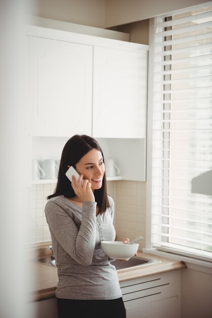 Woman talking on smart phone while holding food bowl