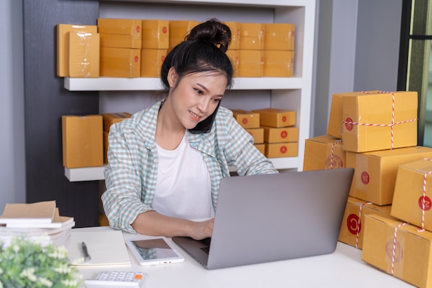 Woman talking on smartphone and use computer laptop to selling product online from home office