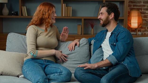 Woman talking with man at home joyful caucasian couple sit on couch redhead girl telling funny story