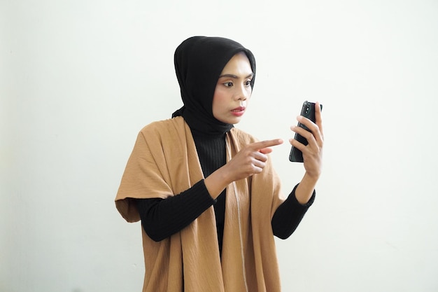 A woman in a tan jacket is holding a phone and pointing at the screen.