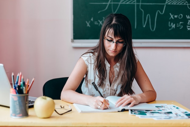 Insegnante della donna in vetri che scrive mentre seduto al tavolo.