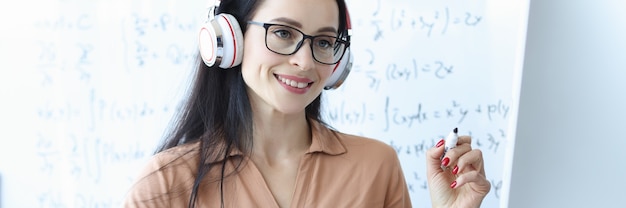 Woman teacher in headphones looking at computer screen on background of blackboard