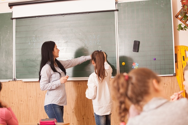 Foto insegnante donna che aiuta l'allievo a risolvere un esempio di matematica alla lavagna