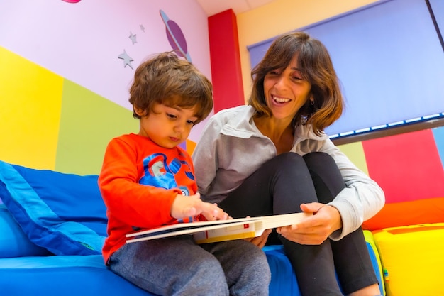Woman teacher playing with a child sitting reading a book and having fun interior of a kindergarten