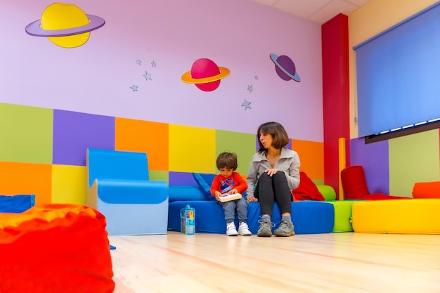 Foto insegnante donna che gioca con un bambino seduto a leggere un libro al coperto di un asilo