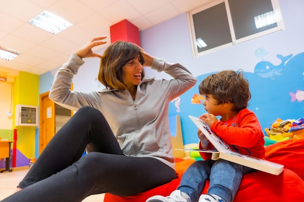 Foto insegnante donna con un bambino seduto a leggere un libro ed esprimere cose dalla storia all'interno di un asilo