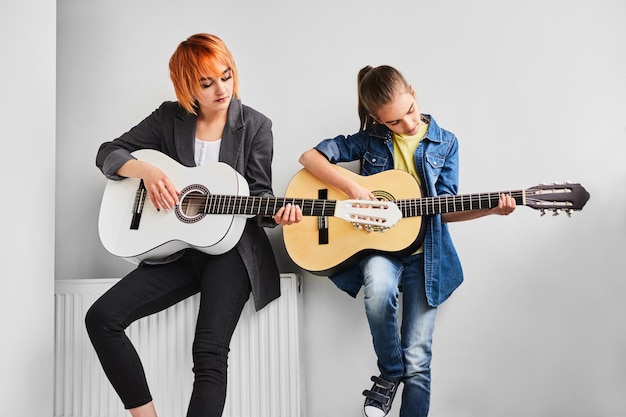 Woman and teenager playing guitars near wall