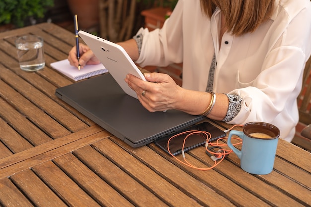 Woman teleworking and taking notes in a notebook from the garden of her house.