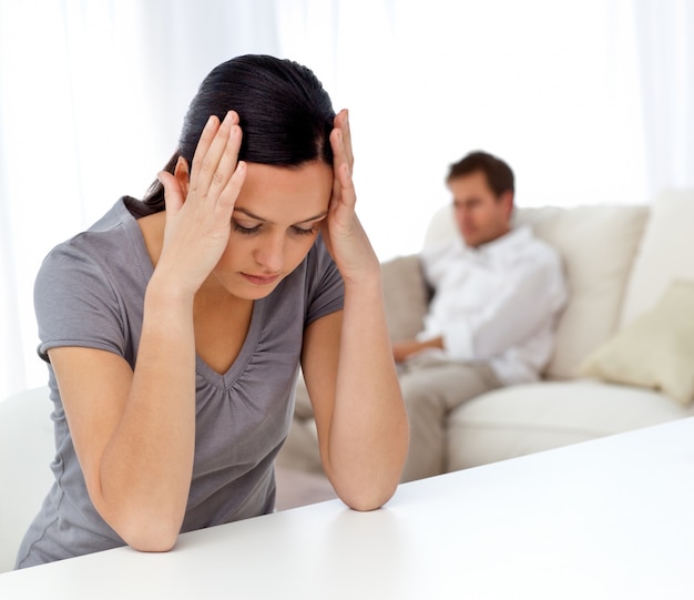 woman thinking at a table while her boyfriend relaxing on the sofa