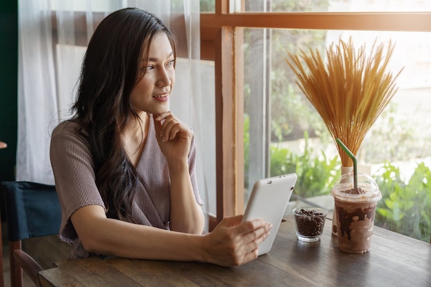 Woman thinking and using tablet in cafÃ©