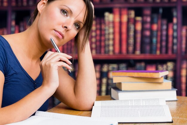 Foto donna che pensa con la penna e prenota in biblioteca