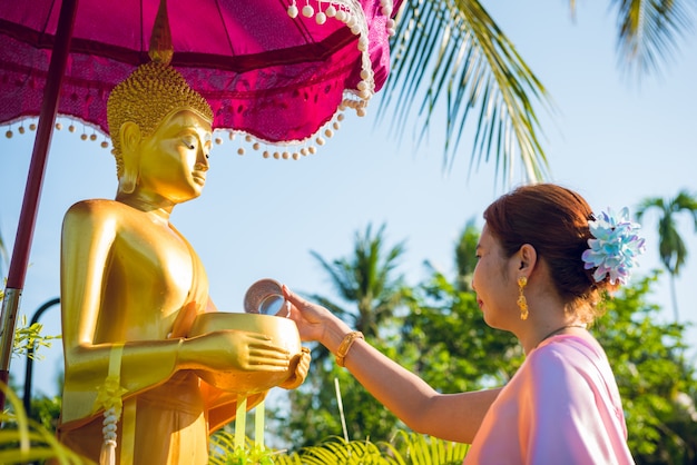 Una donna che indossa abiti tradizionali tailandesi sta versando acqua sulla statua del buddha in occasione del giorno del festival di songkran
