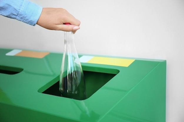 Woman throwing glass bottle into litter bin outdoors