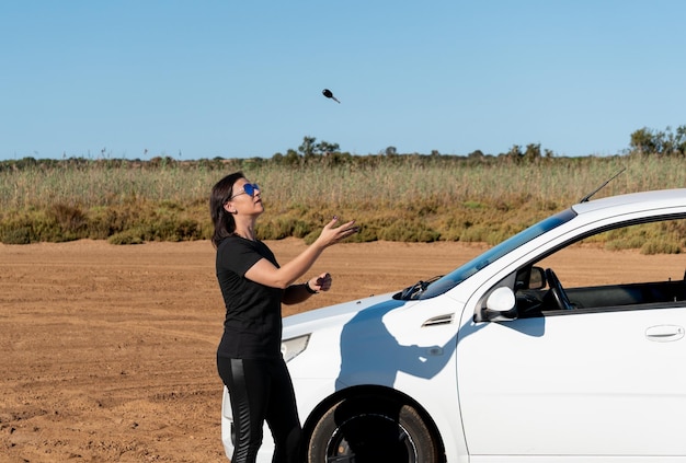 未舗装の道路で車のキーを空中に投げる女性