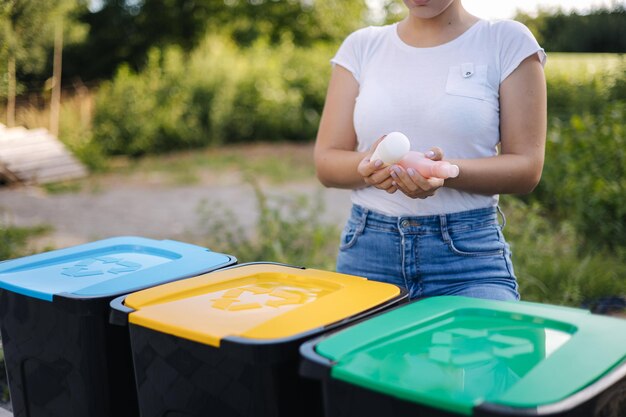 Woman throwing out in recycling bin washed and empty shampoo and deodorant bottles female looks at