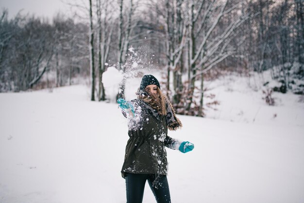 Foto donna che lancia neve contro gli alberi nudi