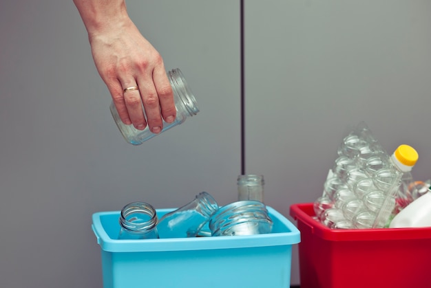 The woman throws the glass bottle to the one of four container for sorting garbage