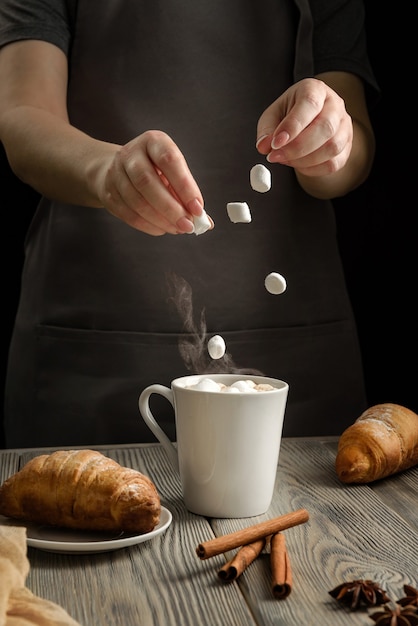A woman throws marshmallows into a cup of cocoa.