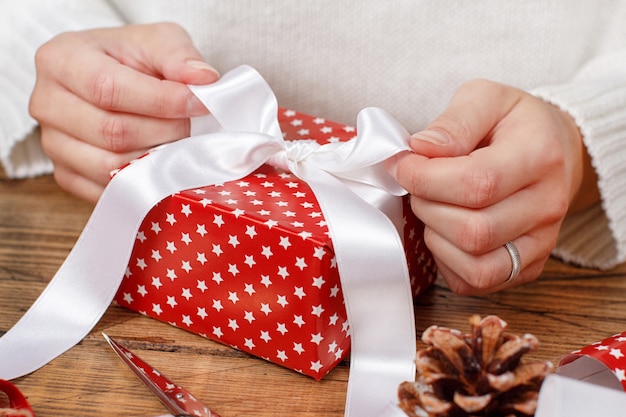 Woman ties a ribbon bow on a wrapped present close up