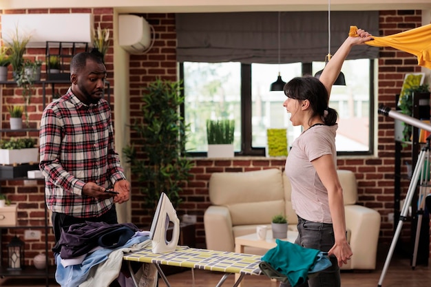 Woman tired of doing all the chores at home without help while husband is distracted by cell phone. African American man trying to communicate with his wife and solve problems by talking.