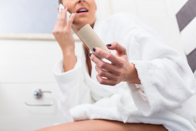 Woman on toilet complaining via phone about lack of paper