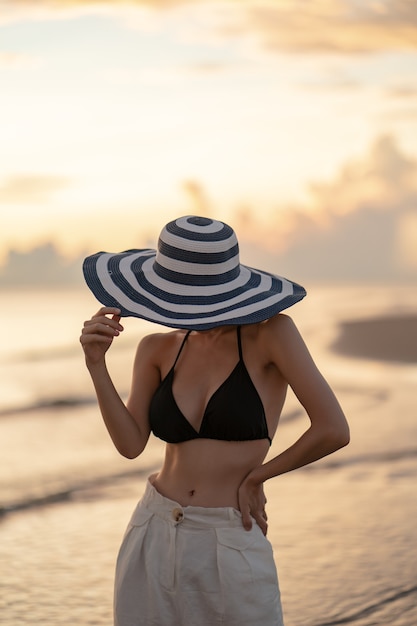 Woman in top bikini and white long pant wearing hat