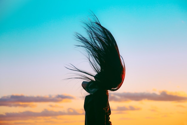 Photo woman tossing hair against sky during sunset