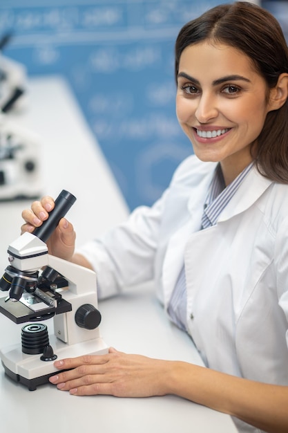 Woman touching microscope smiling at camera