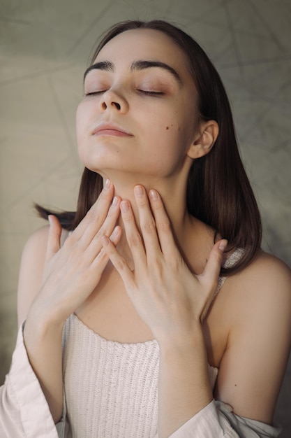 Woman touching neck and applying moisturizing cream while doing skin care beauty routine at home