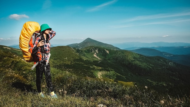 Woman tourist is walking on a hiking trail with a backpack against background of mountains and sky