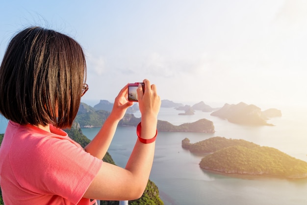 Woman tourist on peak viewpoint of Ko Wua Ta Lap island use camera take photos at beautiful nature landscape during sunrise over the sea in Mu Ko Ang Thong National Marine Park, Surat Thani, Thailand